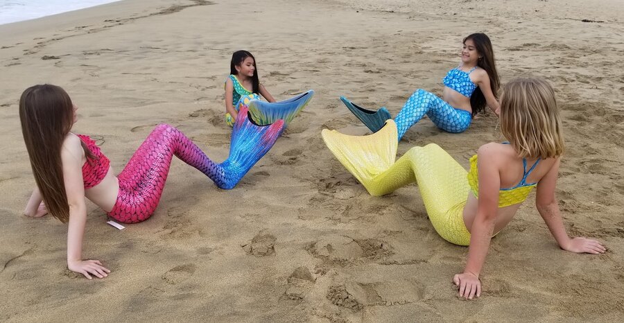 Group of mermaid tails in pink, blue, and yellow on the beach