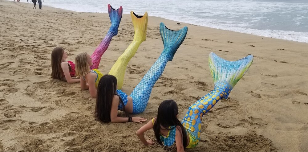 Row of mermaid tails lying on the beach, pink blue yellow and green