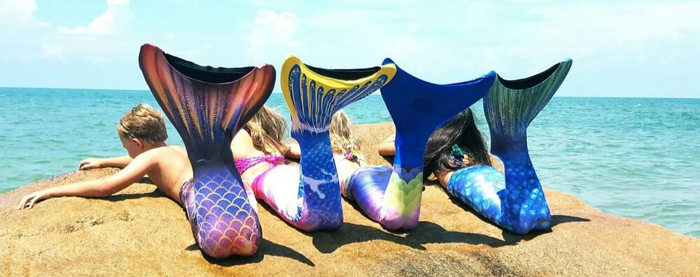 Row of four mermaid tails in different colorways on a rock by the ocean